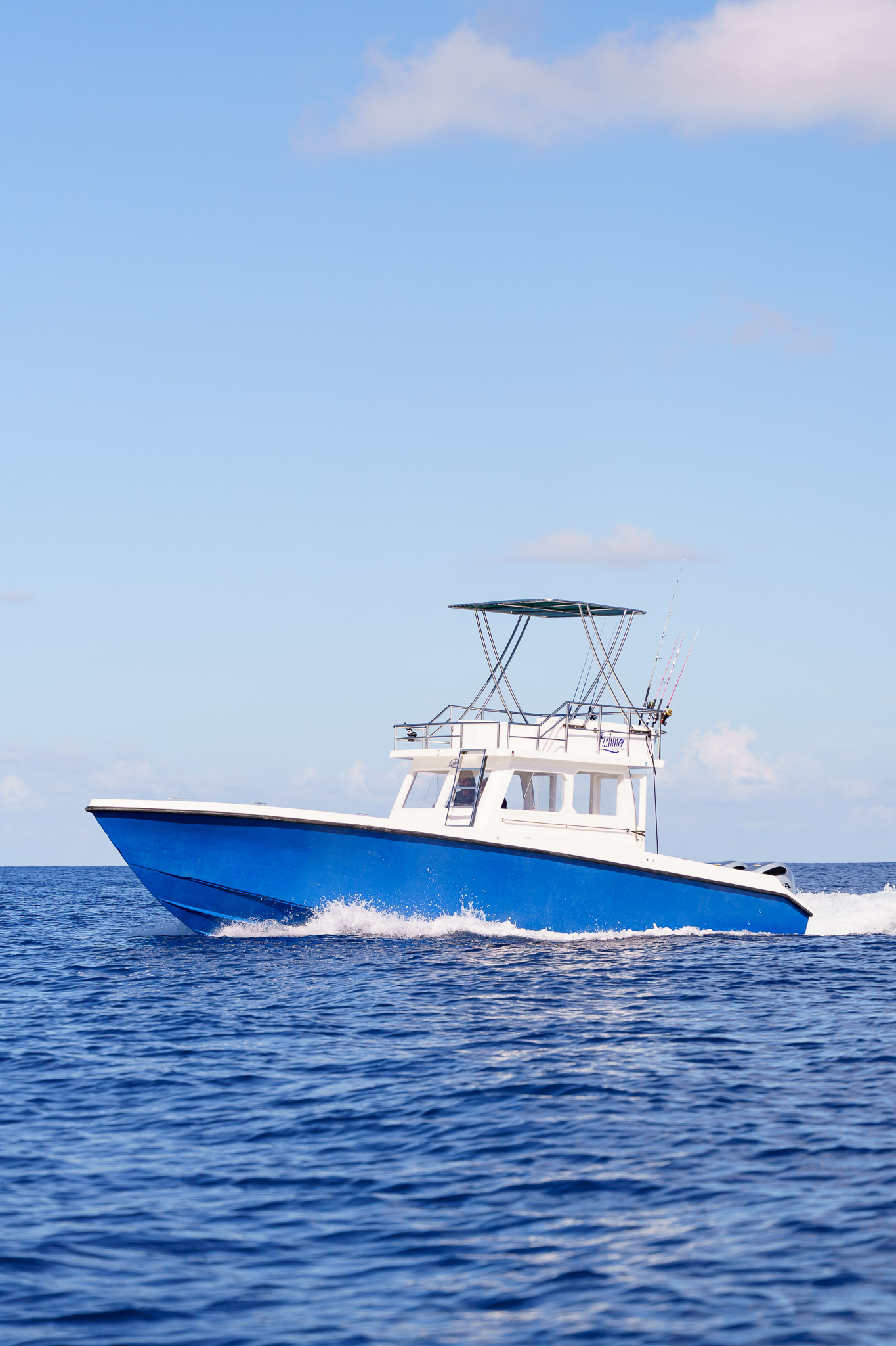 Offshore cabin cruiser with T-top and twin outboards running at speed